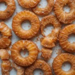 Crispy fried pineapple rings coated in brown sugar and cinnamon on a white surface.